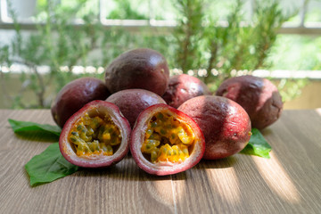 Fototapeta na wymiar A group of purple skin passionfruit plant, sliced and round fruits under sunlight morning on wooden table, blurred background
