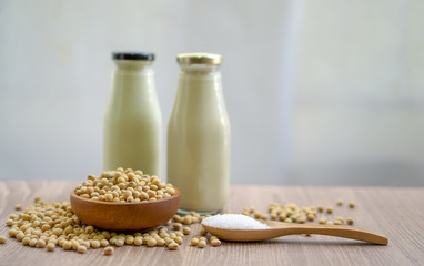 Fresh soybean seeds in brown wooden bowl with sugar in spoon and two bottles of soy milk on the table,  under sunlight morning blurred background, delicious healthy drinking for breakfast