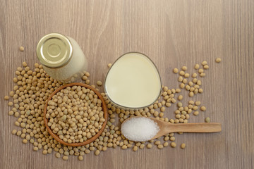 Top view, fresh soybean seeds in brown wooden bowl with sugar in a spoon, a bottle and a glass of soy milk on the wood table, delicious healthy drinking for breakfast