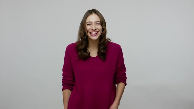 Happy overjoyed nice-looking brunette woman in pullover holding stomach and laughing out loud, almost crying with hilarious laughter, amused by really funny joke. indoor studio shot gray background