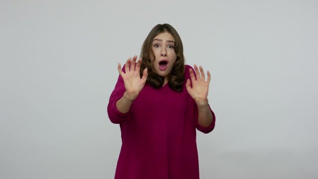 Phobia. Frightened brunette woman in pullover shaking and screaming from fear, freaked out gesturing to defend herself, looking terrified and scared. indoor studio shot isolated on gray background