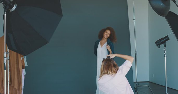 Young professional studio photographer taking photos of an african american fashion model in front of a blue seamless with multiple flashes, high end fashion photoshoot behind the scenes