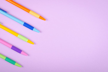 Different colored pens, school ballpoint on purple background composition.