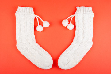 White socks with pom poms on red background composition.