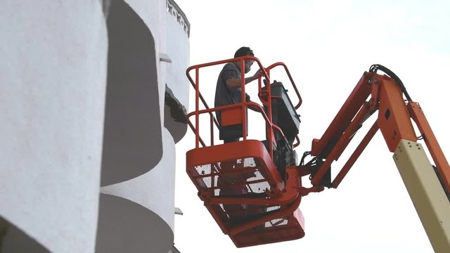 Mature man on a telescopic boom lift platform approaches a wall in to make repairs, in slow motion. Work concept.