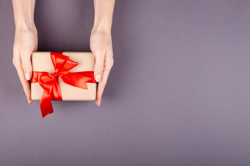 Hands with gift box on dark background composition, present with ribbon and bow.