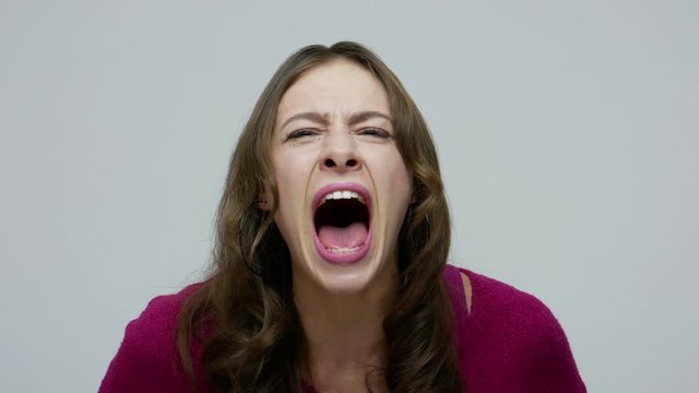 Mad scream. Closeup of furious brunette woman shouting loudly, yelling aggressively with crazy face, feeling pissed off, expressing rage anger and hate. indoor studio shot isolated on gray background