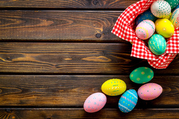 Basket with painted eggs for Easter dinner on dark wooden desk top-down copy space