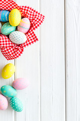 Easter eggs painted in basket on white wooden desk top-down copy space
