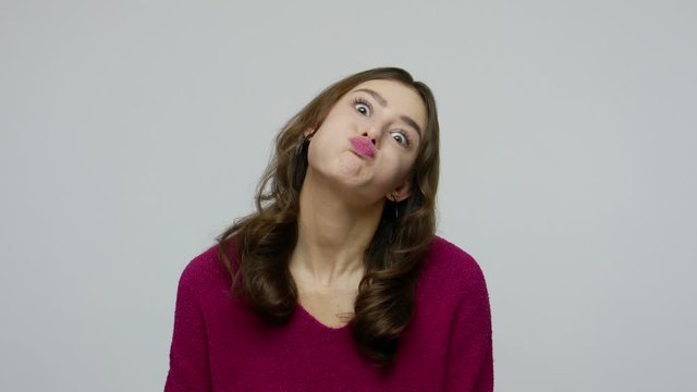 Naughty childish brunette woman in pullover showing tongue to camera and making fish face, having fun with duck grimace, idiotic foolish expression. indoor studio shot isolated on gray background