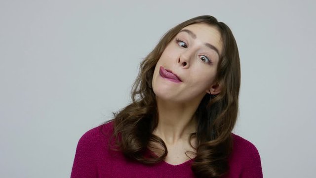 Closeup of carefree funny comical brunette woman making humorous face with eyes crossed, playing fool, having fun with stupid dumb brainless expression. indoor studio shot isolated on gray background