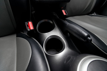 Interior view with leather seats , two cup holders, red safety belt locks and arm brake of black used car stands in the showroom after dry washing before sale