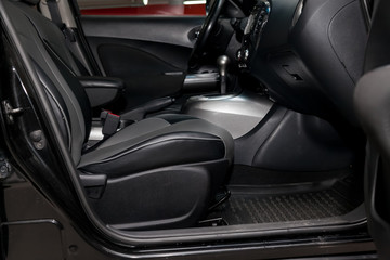 Comfortable front seats inside the car: the driver and passenger, tied with black leather, modern interior design, the steering wheel covered and a luxurious center console.