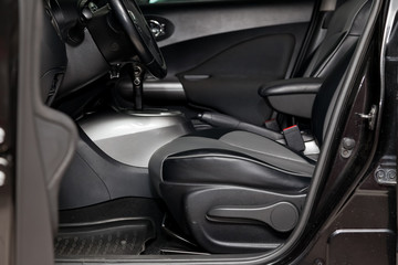 Comfortable front seats inside the car: the driver and passenger, tied with black leather, modern interior design, the steering wheel covered and a luxurious center console.