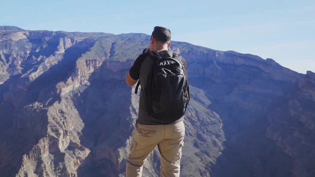 Young Foreign Male Tourist Taking Photos on Professional Camera of Wadi Ghul aka Grand Canyon of Oman in Jebel Shams Mountains. Man in Active Solo Travel in Middle East Countries