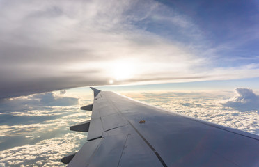 Obraz premium Sky scape view from clear glass window seat to the aircraft wing of the plane, traveling on the clouds and sunshine with blue sky
