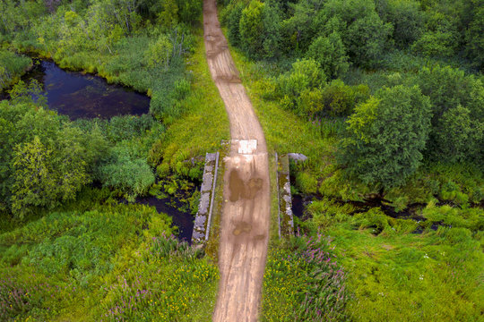 Top view of a country road and the collapsing old bridge over an overgrown river