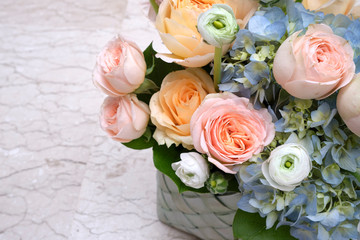 A bouquet of fresh flowers of roses, anemones and gartensium in a basket on a stone background.
