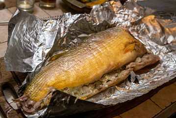 Homemade grilled dorado fish with vegetables wrapped in aluminum foil on rustic table. Top view.