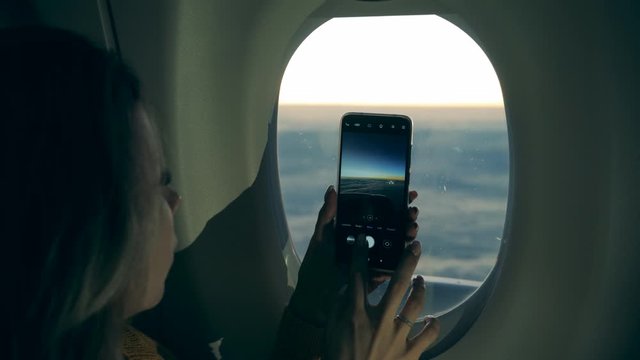 A cellphone in woman's hands while taking pictures on the plane