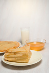 Maslenitsa is a holiday at the end of February . pancakes with honey and milk on a light wooden background. honey trickles down a stack of pancakes. close up. blini. space for text. vertical photo