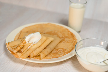 Maslenitsa is a holiday at the end of February . pancakes with sour cream and milk on a light wooden background. close up. blini. space for text.