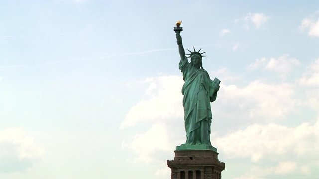 The majestic Statue of Liberty holding her torch and tabula ansata with white clouds as background. Tracking low angle. Full shot.
