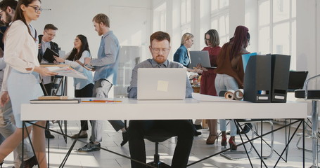 Camera zooms in on exhausted young businessman throwing paper documents in the air at busy modern office table RED EPIC.