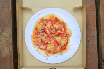 Pizza in cardboard paper box on wooden table. Top view.