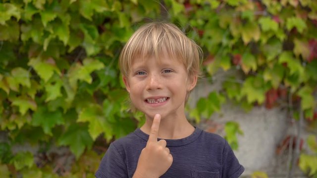 A little boy shows his milk tooth that is ready to fall off. Slowmotion shot