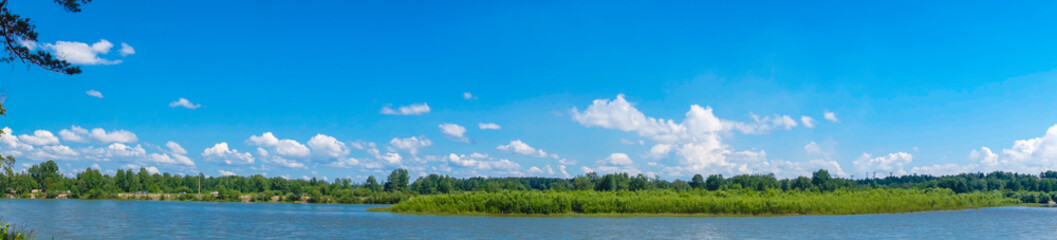 Obraz premium Summer panorama of the river with green trees along the shore. Snow-white clouds on a background of blue sky. Kitoy River Russia.