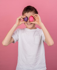 Smiling boy covering eyes with colorful eggs isolated on pink bakground