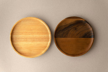 Top view above empty dark brown split stained acacia or teak wooden renewable serving plate next to light brown bamboo wooden plate on soft plain grey organic paper isolated background.