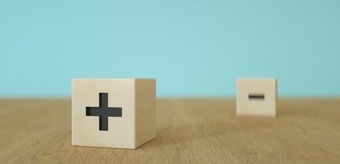 wooden cubes or dice with black plus  foreground and minus sign in the background on wooden table