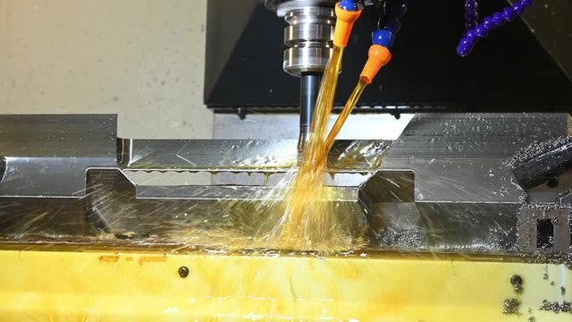 The CNC milling machine rough cutting the mold and die parts with oil coolant. The mold and die manufacturing process by CNC machining center.