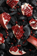 Red fruit slices on a dark texture. Preparation for hookah. Ripe cut pomegranate. Black charcoal background.