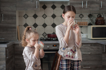 Two girls big and small drink milk in the kitchen