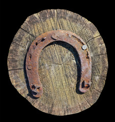 A large rusty horseshoe is nailed to an oak stump isolated black