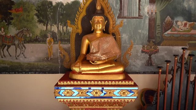 Peaceful golden buddha statue with religious paintings in the background in a Buddhist Temple. Chiang Mai, Thailand.