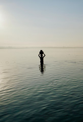 Fototapeta na wymiar silhouette of a boy holding a bamboo jar above the head, standing in the water at sunrise