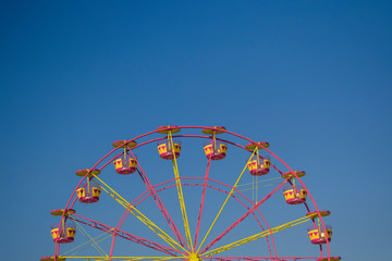 Attraction - Ferris wheel. Colors red yellow. Against the background of blue sky. No people.