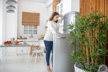 Dark-haired woman in a striped blouse opening the fridge
