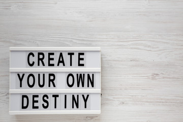 'Create your own destiny' words on a lightbox on a white wooden background, top view. Overhead, from above, flat lay. Space for text.