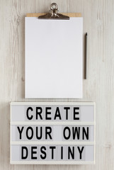 'Create your own destiny' words on a modern board, clipboard with blank sheet of paper on a white wooden background, top view. Overhead, from above, flat lay. Copy space.