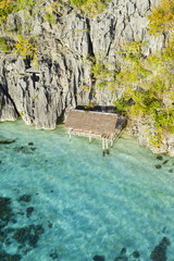 View from above, stunning aerial view of a bungalow surrounded by rocky cliffs bathed by a turquoise, crystal clear sea. Malwawey Coral Garden, Coron Island, Palawan, Philippines.