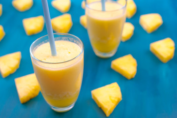 fresh pineapple juice in a glass with a straw on a blue and green background