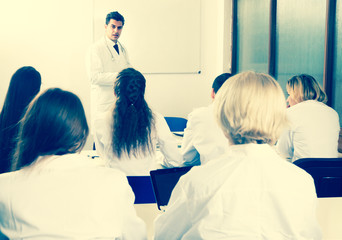 Students in white coats listen to lecture in audience
