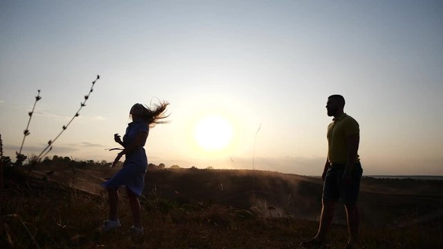 Side view of a beautiful young girl runs up and bounces to her boyfriend and begins to kiss and hug with him against the background of the evening sunset in slow motion. Happy and long relationship.