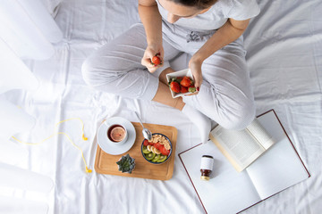 Young woman eating healthy breakfast in bed.