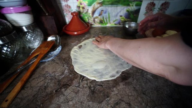 The most traditional Moroccan dishes. Moroccan woman spreading the ball dough in a circle using her hands, on a marble counter.  making Rfissa